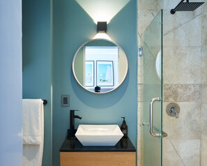 Un bagno con uno specchio rotondo, un lavandino bianco e uno spazio doccia in vetro.