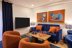 Ein modernes Wohnzimmer mit einem blauen Sofa, orangefarbenen Sesseln und einem Flachbildfernseher.