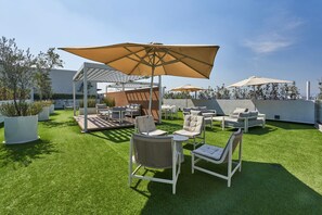 Eine Außenpatio mit Kunstgrasanlage, weißen Möbeln und großen Sonnenschirmen.