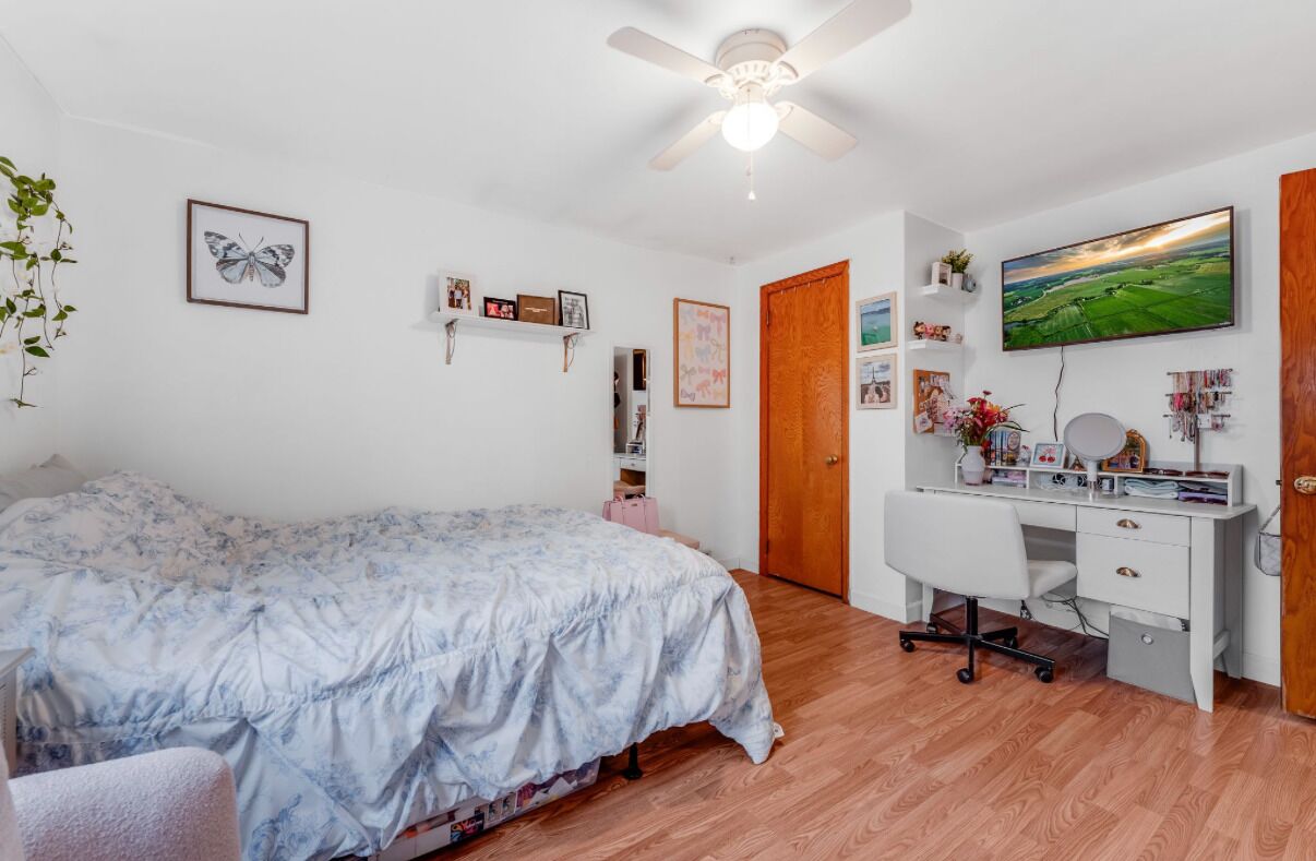 Un dormitorio con cama, escritorio, silla, ventilador de techo y puerta.