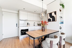 A modern kitchen with white cabinets, a wooden dining table, and a vase of red flowers. - GuestReady - Chic Riverside Apartment Retreat (Vila Nova de Gaia)