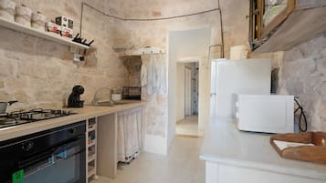 A kitchen with a stove, oven, and white refrigerator. There is a shelf with boxes and a hanging rack with cloths.