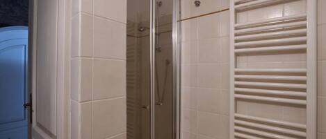 Une salle de bain avec une douche à parois de verre, des murs recouverts de carreaux blancs et un porte-serviettes.