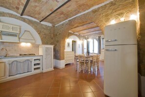 A kitchen with a stone archway, a white refrigerator, and a dining area with wooden chairs. - Podere San Giuseppe (Toscana)
