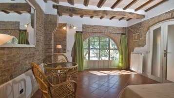A room with a brick wall, a round table with chairs, a window with curtains, and a door.