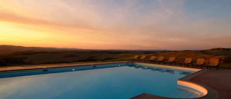 A swimming pool with a curved edge, surrounded by lounge chairs and a view of rolling hills.