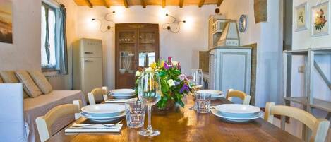 A dining area with a wooden table set for four, surrounded by chairs. There is a buffet counter with a refrigerator and a cabinet in the background.