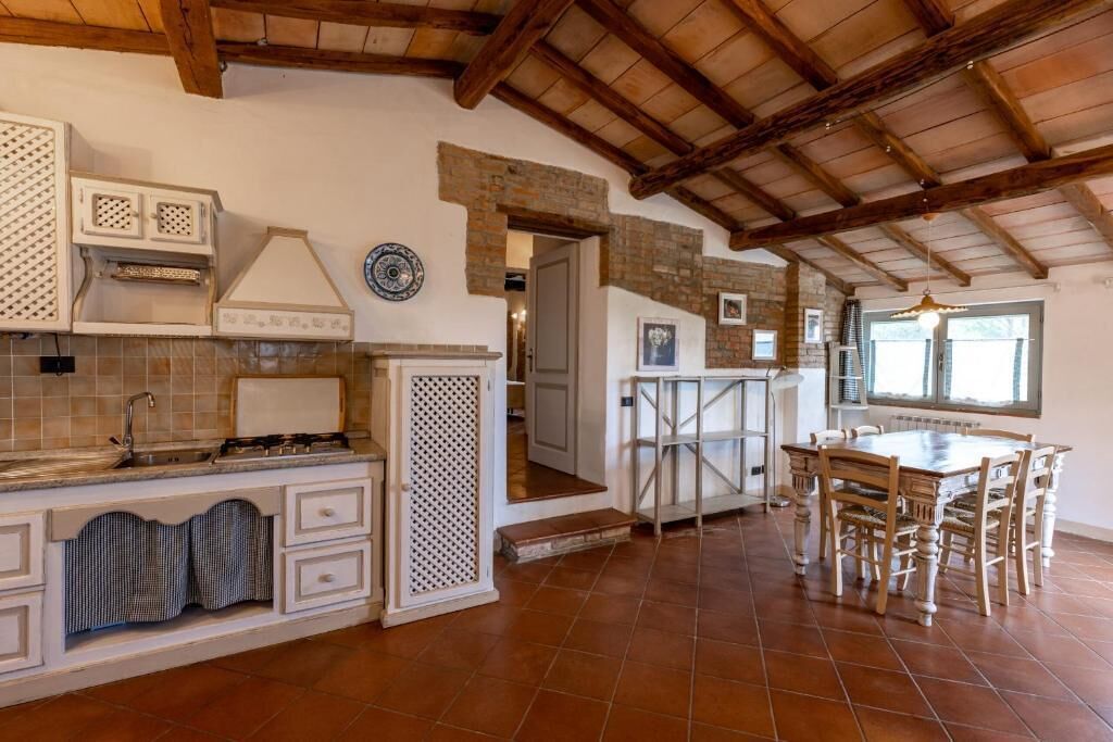 A kitchen with a tiled floor, wooden ceiling beams, a dining table with chairs, and a built-in oven.