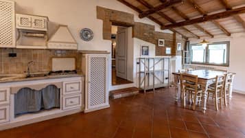 A kitchen with a tiled floor, wooden ceiling beams, a dining table with chairs, and a built-in oven.