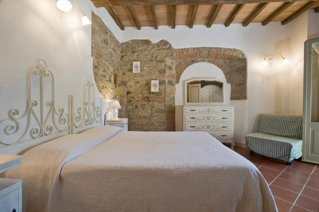 A bedroom with a stone wall, a bed with a headboard, a dresser, and a chair.