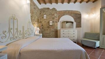 A bedroom with a stone wall, a bed with a headboard, a dresser, and a chair.