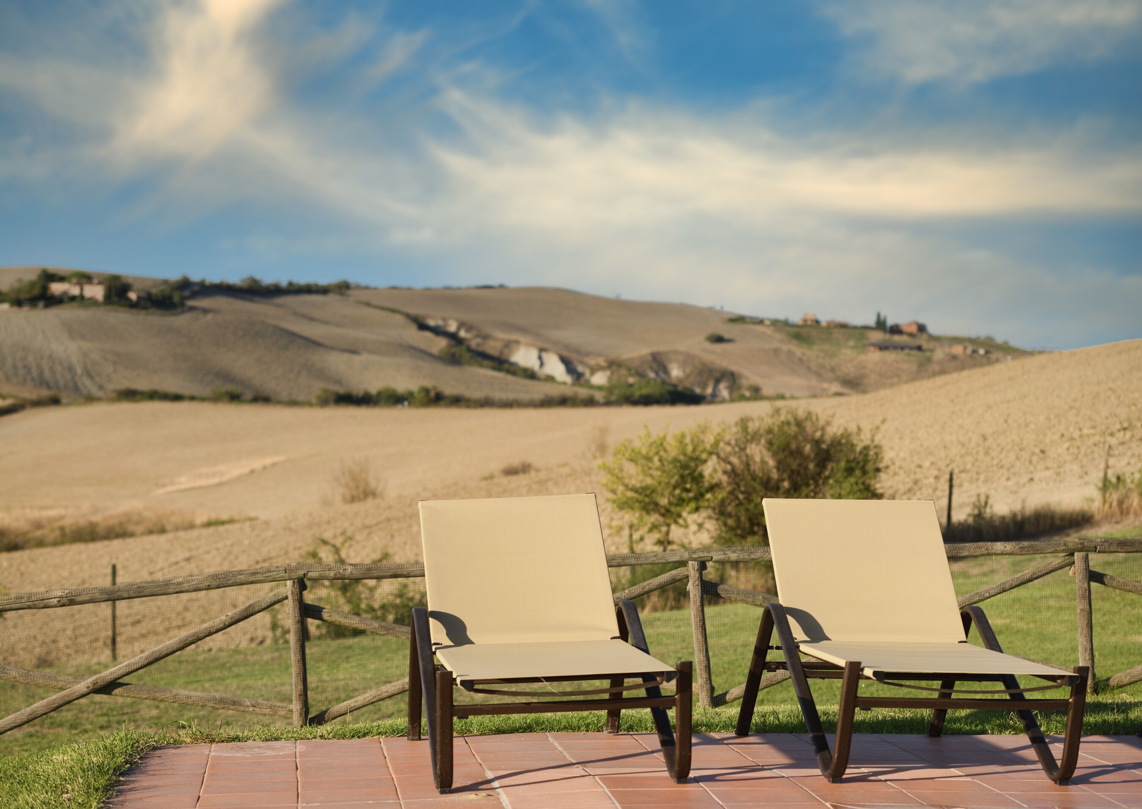 Two lounge chairs on a brick patio with a view of rolling hills and a clear sky.