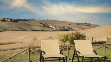 Two lounge chairs on a brick patio with a view of rolling hills and a clear sky.