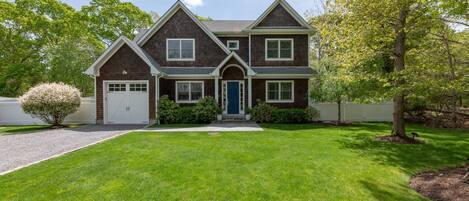 A two-story house with a front garage, a well-maintained lawn, and mature trees.