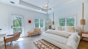 A bedroom with a large bed, a desk, a chair, and a window.