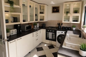 Eine kleine Küche mit weißen Schränken, einer schwarzen Arbeitsplatte, einer Mikrowelle, einem Toaster, einem Herd, einer Waschmaschine und einem Spülbecken.