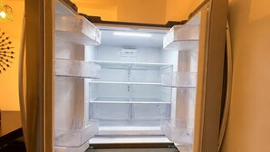 A compact refrigerator with multiple shelves and a freezer compartment, situated in a room with wooden flooring and a wall-mounted light fixture.