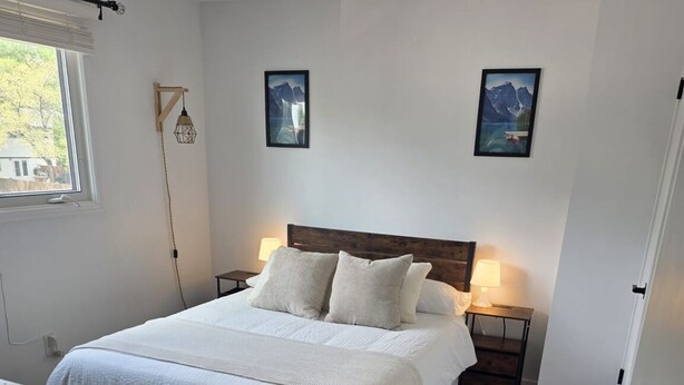 A bedroom with a bed, bedside lamps, a window, and a door.