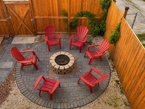 Zona de estar al aire libre circular con sillones Adirondack rojos alrededor de una chimenea central.