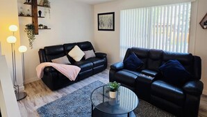 A living room with two black leather sofas, a round coffee table with a plant, a grey shag rug, and a floor lamp.