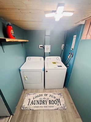 Un cuarto de lavandería con dos lavadoras, un estante con una botella y un letrero en la pared.