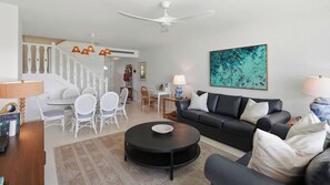 A modern living room with a black leather sofa, a round coffee table, and a dining area with white wicker chairs. - Awesome Beach Condo on Perfect Seven Mile Beach! (Seven Mile Beach)