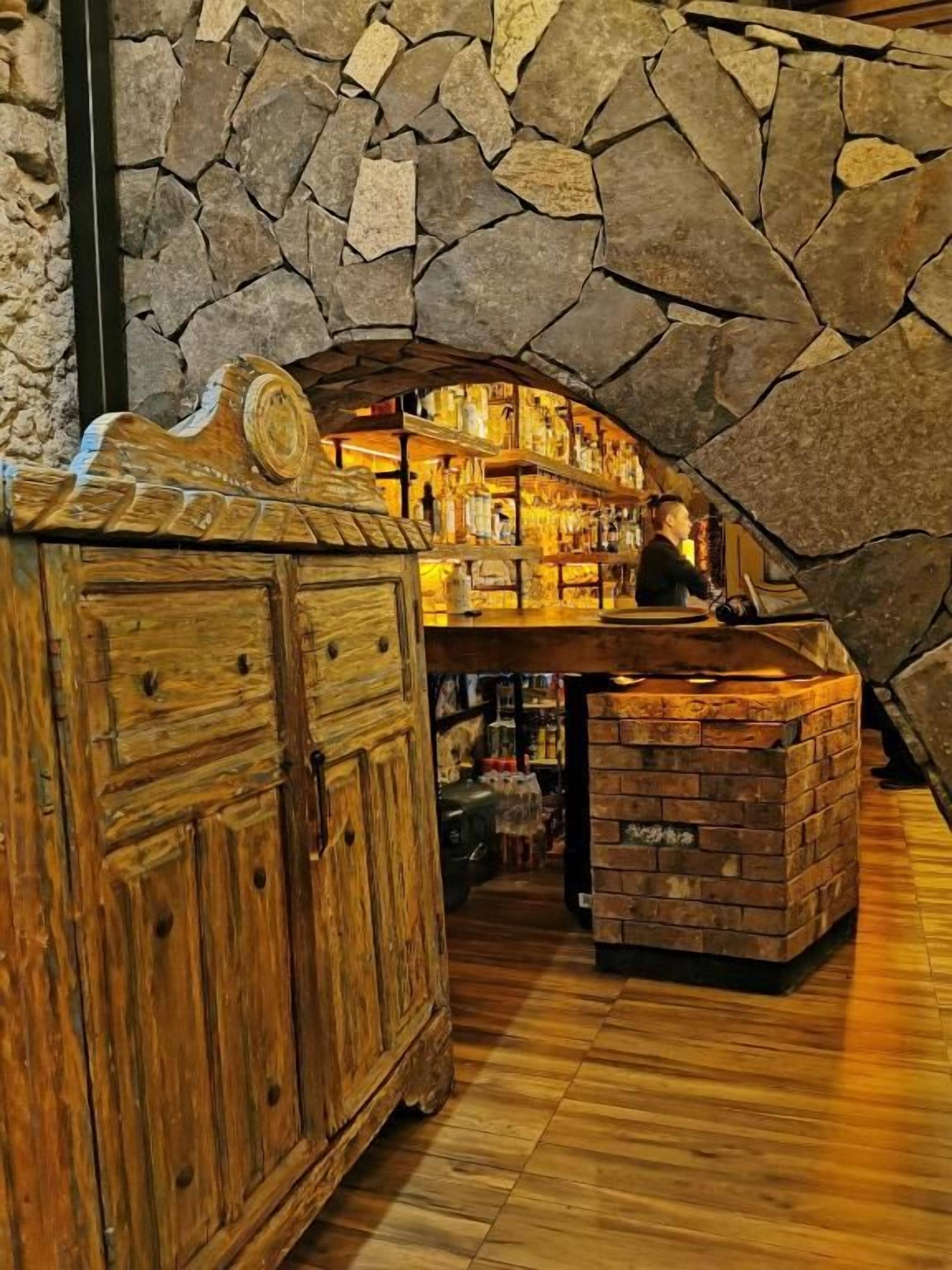 Een bar met een stenen muur, een houten toonbank en flessenkasten.