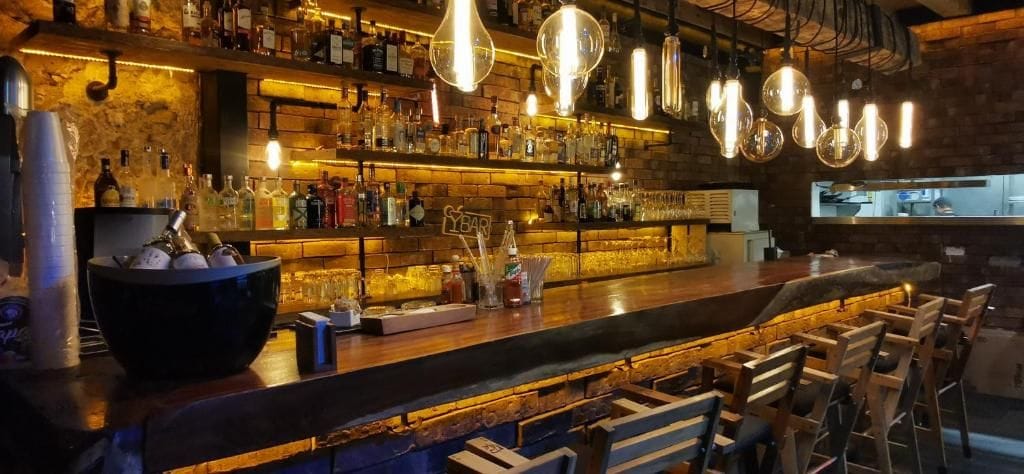 Een bar met een houten toonbank, barstoelen en verschillende flessen en glazen.