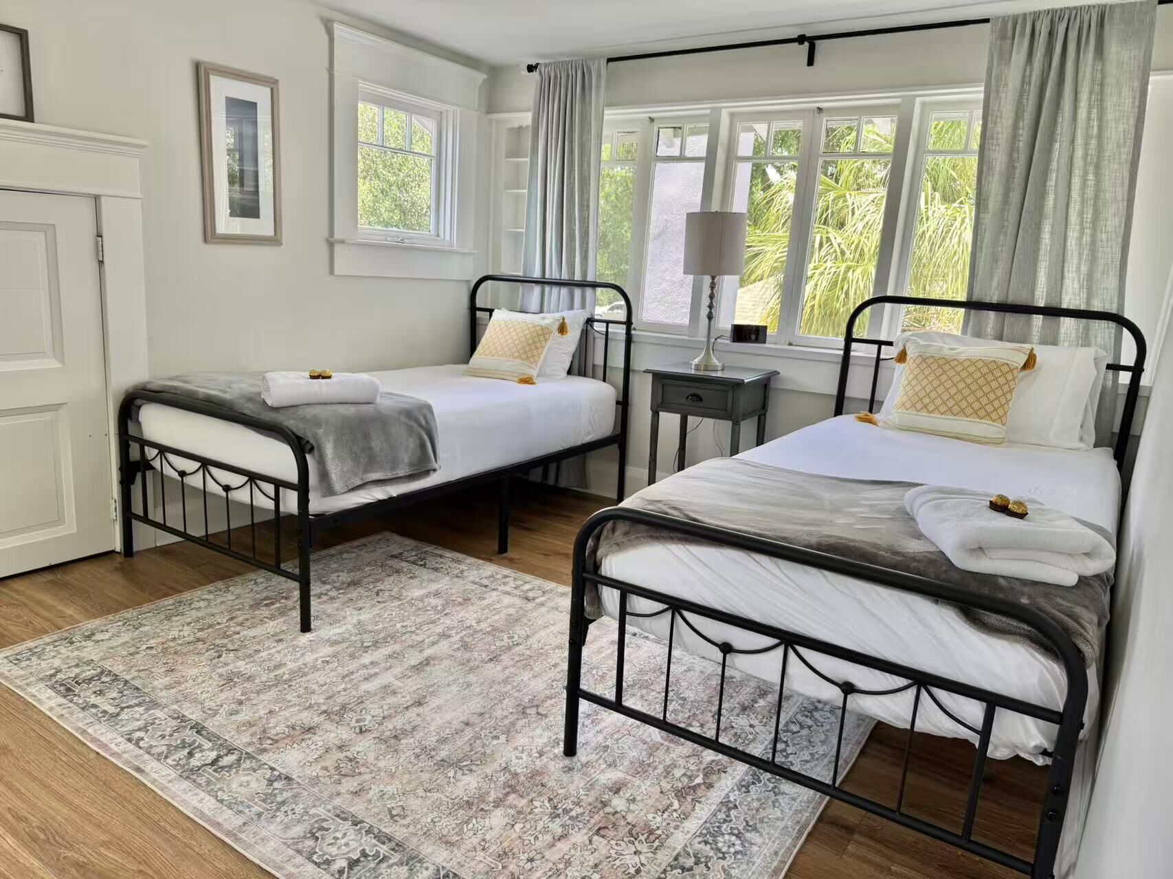 Une chambre avec deux lits simples, une table de chevet avec une lampe, une fenêtre avec des rideaux et un tapis à motifs.