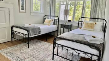 Une chambre avec deux lits simples, une table de chevet avec une lampe, une fenêtre avec des rideaux et un tapis à motifs.