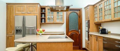 Una cocina con gabinetes de madera, un refrigerador de acero inoxidable, un horno empotrado e una isla central con taburetes.