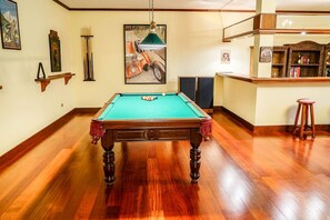 Une table de billard dans une pièce au plancher en bois, un coin bar avec des tabourets et des décorations murales.