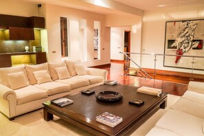 Ein modernes Wohnzimmer mit einem beigefarbenen Sofa, einem Couchtisch mit Zeitschriften und einer Treppe, die in eine weitere Ebene führt.