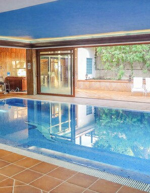 Une piscine intérieure avec des parois en verre transparent, un intérieur en bois et une vue sur l’extérieur.