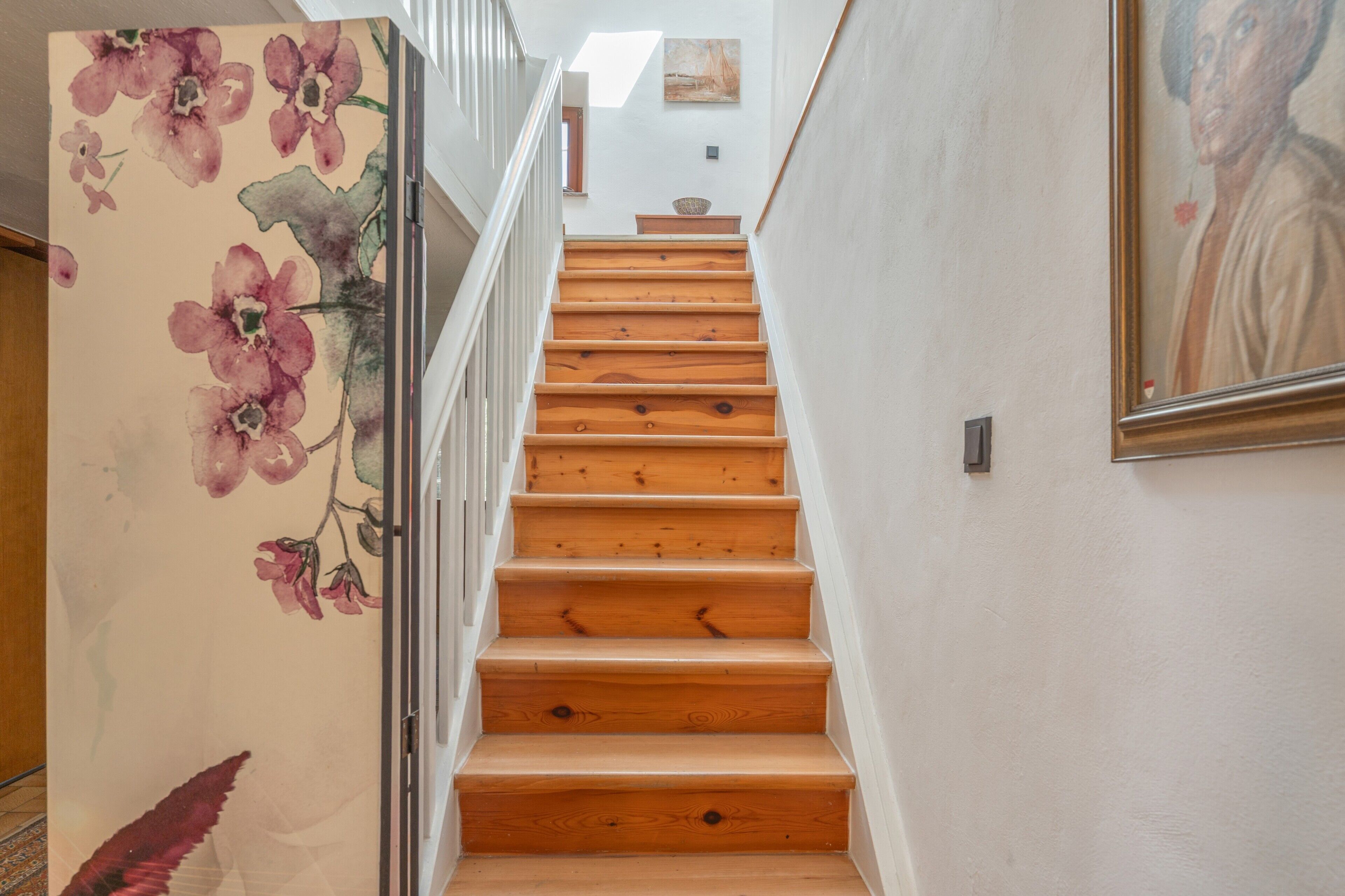 A wooden staircase with white walls and a floral mural on the left.