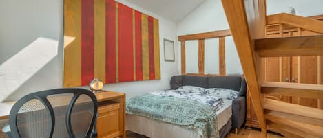 A bedroom with a sloped ceiling, a desk, a chair, a bed, and a wooden bunk bed.