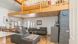 A spacious living area with a high ceiling, wooden beams, a dining table, and a sofa. - Holiday Apartment in Kipfenberg – 1 Bedroom / Sleeping Gallery / 2 Bathrooms (Kipfenberg)