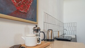 A kitchen area with a coffee maker, kettle, and a white mug on a wooden countertop. - Holiday Apartment in Kipfenberg – 1 Bedroom / Sleeping Gallery / 2 Bathrooms (Kipfenberg)