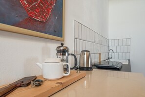 En köksdel med en kaffebryggare, vattenkokare och en vit mugg på en bänkskiva i trä.