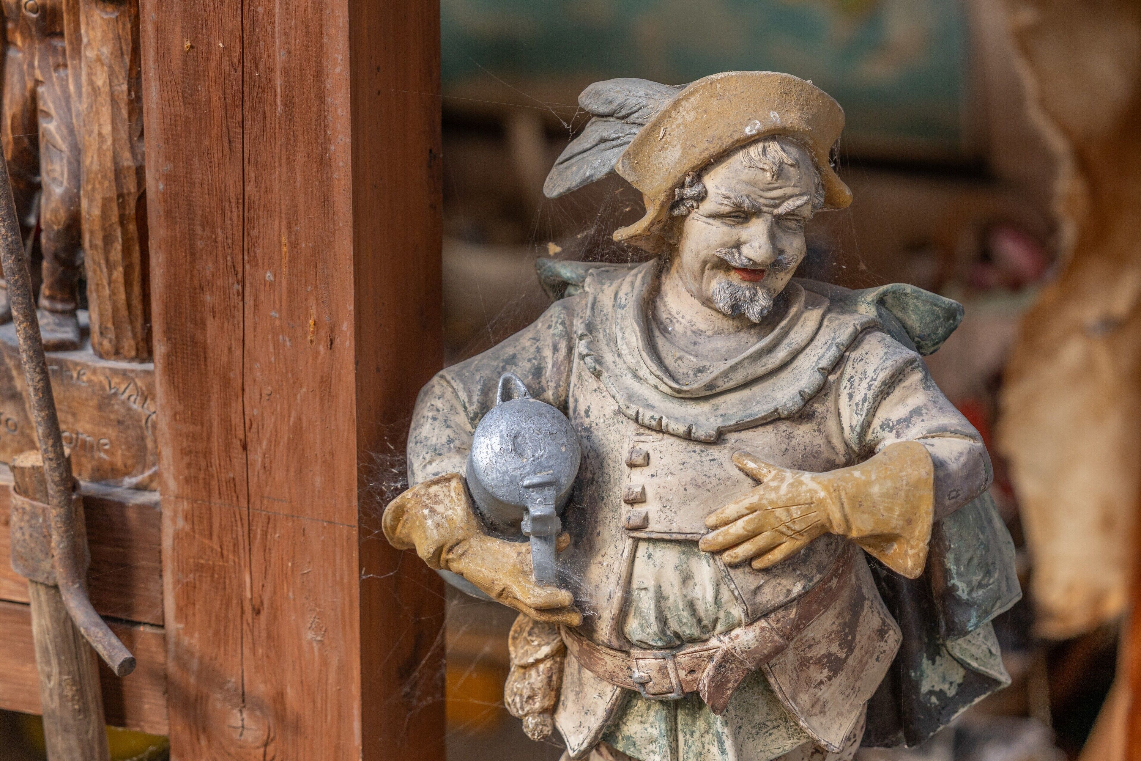 Een standbeeld van een figuur die een kan vasthoudt, voor een houten constructie geplaatst.