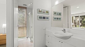 Un bany modern amb un mirall gran, un lavabo blanc i una finestra amb persianes.