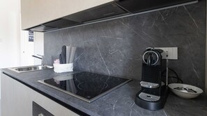Una cocina moderna con tope de inducción negro, máquina de espresso integrada y protector de salpicaduras de mármol.