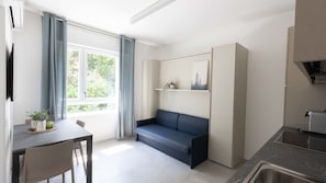 Un espacio habitable compacto con comedor, sofá, zona de cocina y ventana con vistas a zonas verdes.