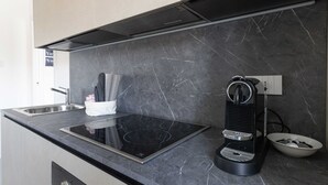 Moderni keittiö, jossa on musta induktiotaso, sisäänrakennettu espressokone ja marmorista tehty välitilan seinä.