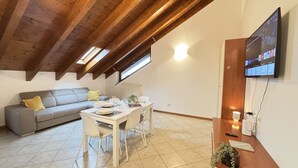 Ein Essbereich mit einem Tisch für vier Personen, einer Couch und einem an der Wand befestigten Fernseher.