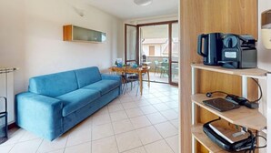 Un salon moderne avec un canapé bleu, une machine à café et un téléviseur à écran plat posé sur une étagère en bois.