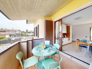A balcony with a table set for dining, chairs, and a view of the neighborhood. - Blue Nest Garda by Booking Lake Garda (Manerba del Garda)
