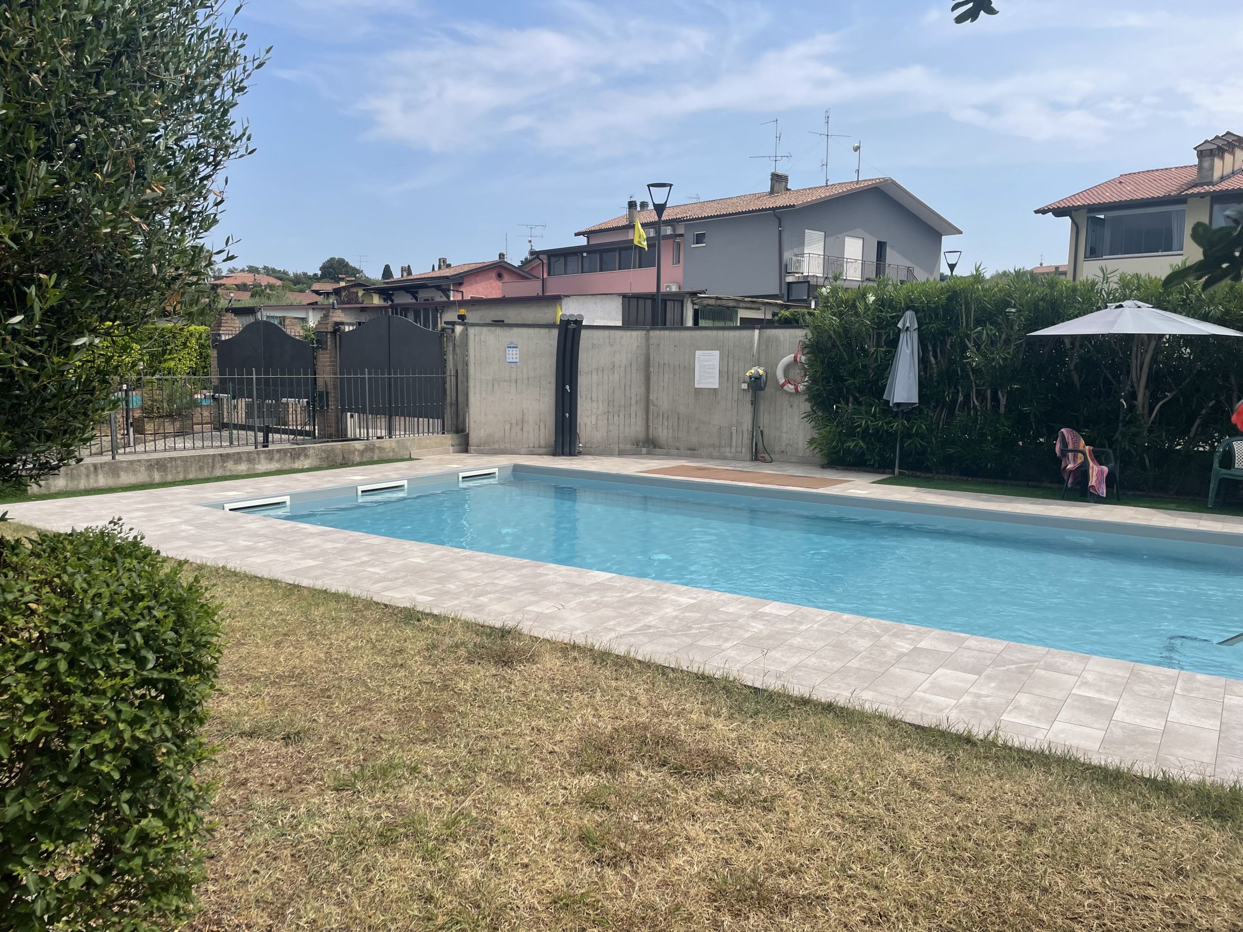 Une piscine rectangulaire dont le bord est recouvert de carreaux, entourée d’une pelouse et d’un petit muret.