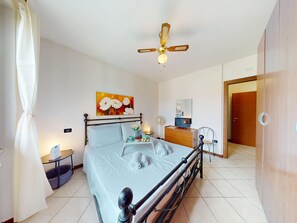 A bedroom with a bed, a ceiling fan, a bedside table, a mirror, and a door. - Blue Nest Garda by Booking Lake Garda (Manerba del Garda)