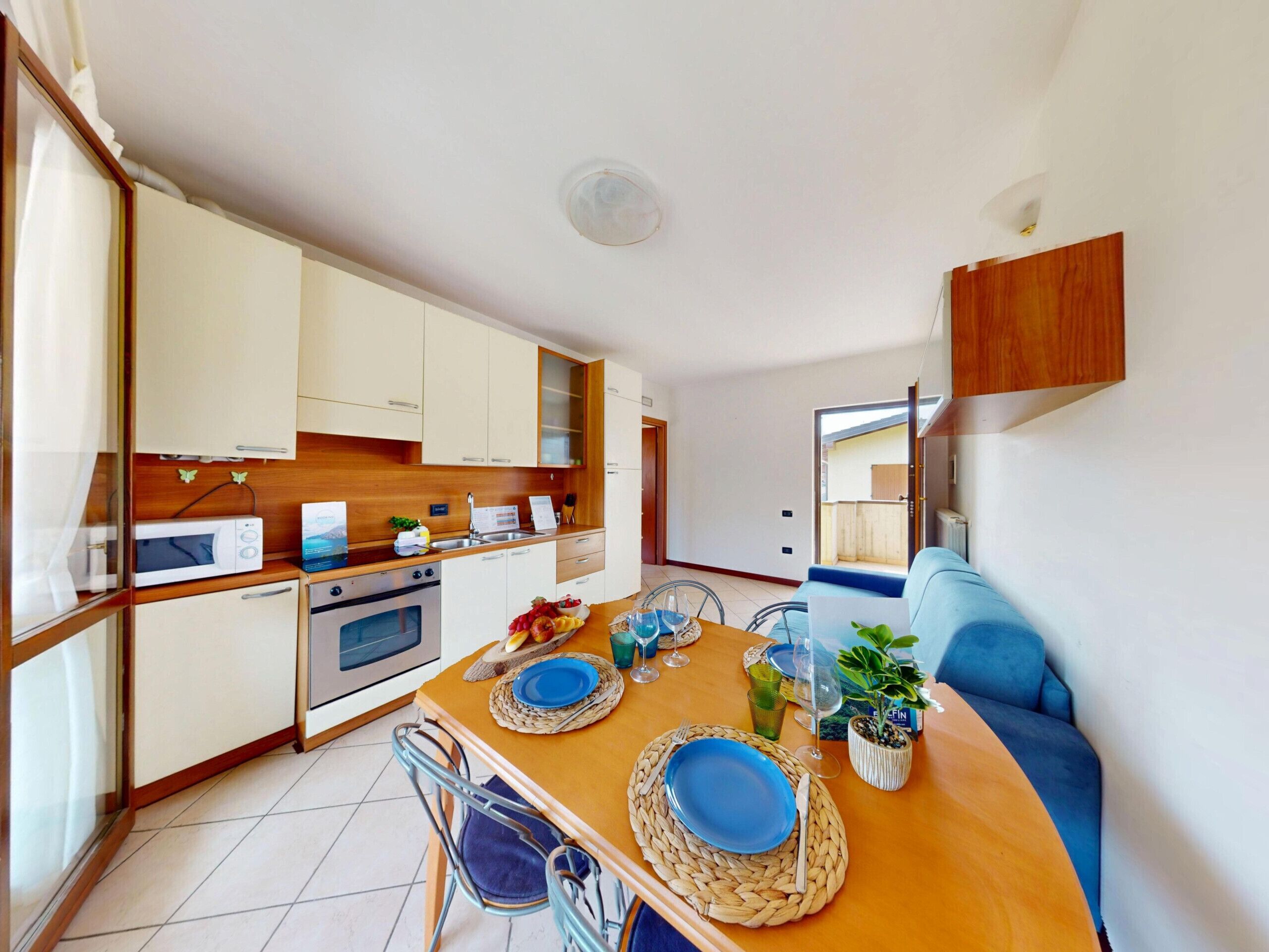 A compact kitchen with modern appliances, a dining area with a wooden table set for two, and a blue sofa.
